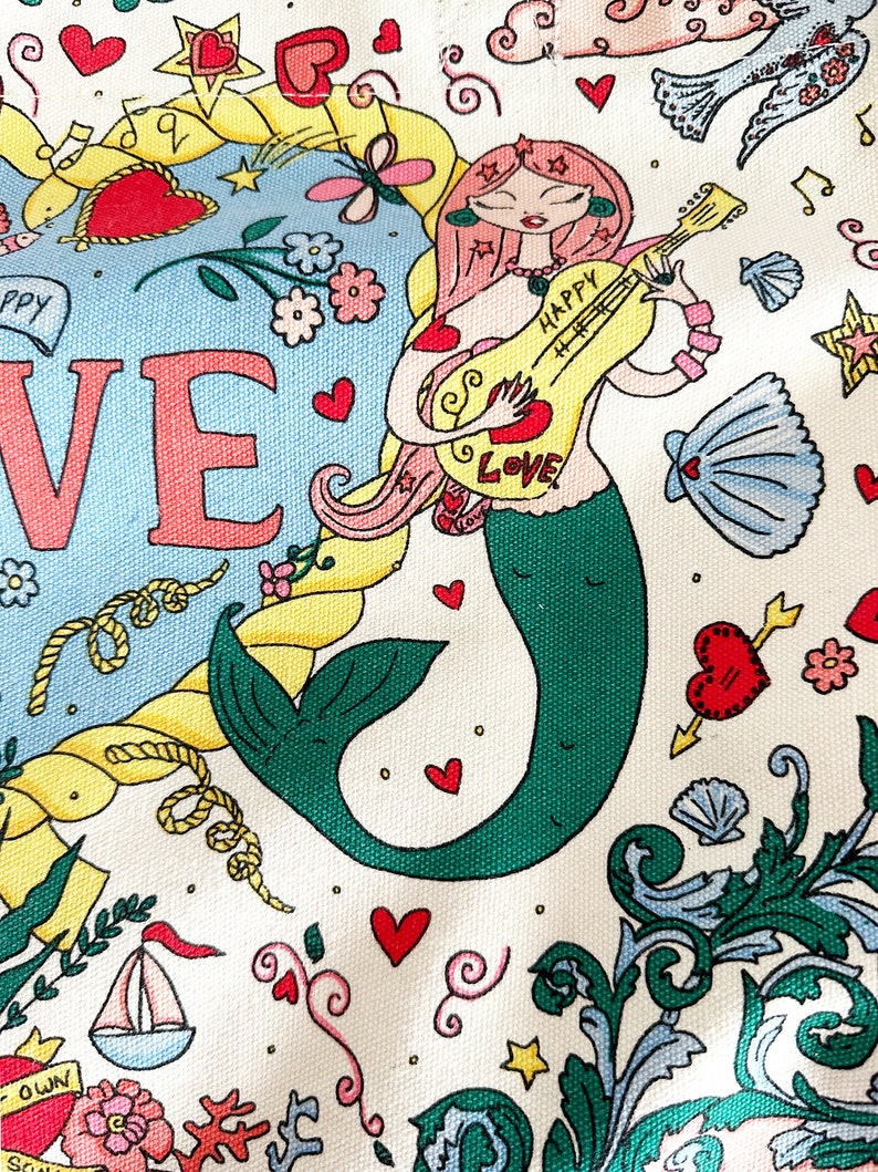 May include: A whimsical illustration featuring a mermaid playing a guitar with the word "HAPPY LOVE" on it. The design includes hearts, stars, musical notes, and nautical elements like a sailboat and rope, all set against a cream background.