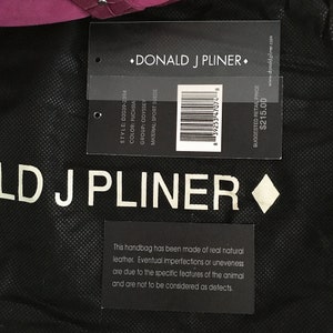 May include: A black handbag with a tag from Donald J Pliner. The tag displays the style, color, group, and material of the bag. The bag is made of real natural leather. The color is fuchsia.