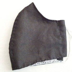 May include: A black face mask with white stitching around the edges. The mask has elastic ear loops.