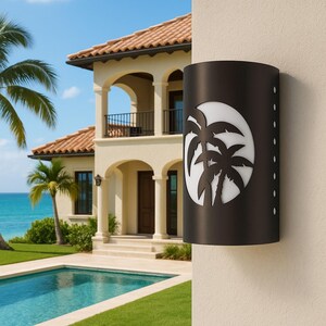 May include: A black outdoor wall sconce with a tropical palm tree design. The cylindrical light fixture has a cut-out pattern of palm trees against a white background. The sconce is mounted on a beige wall next to a house with a pool.