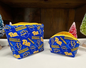 May include: Two blue and yellow zippered pouches with the University of Pittsburgh logo and paw prints. The larger pouch is lying on its side and the smaller pouch is standing upright.