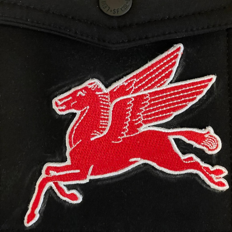 Puede incluir: Parche rojo bordado de un caballo alado, un Pegaso, sobre fondo negro. El caballo est&aacute; corriendo y tiene contornos blancos.