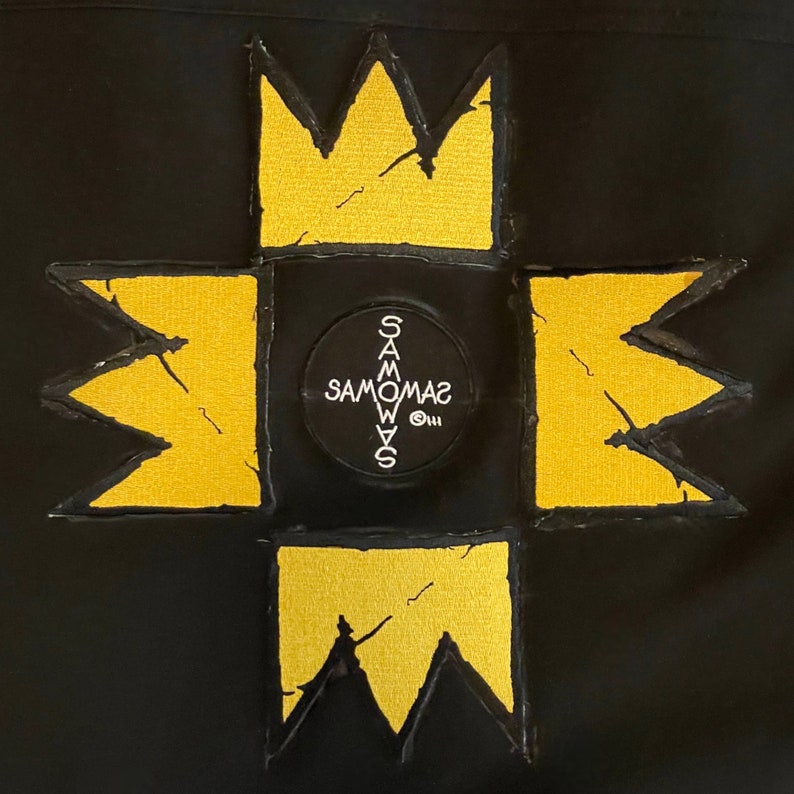 Puede incluir: Un parche de tela negro con un dise&ntilde;o bordado amarillo. El dise&ntilde;o presenta una gran estrella de cuatro puntas con un c&iacute;rculo m&aacute;s peque&ntilde;o en el centro. El c&iacute;rculo tiene el texto "SAMOWAS" escrito en blanco.