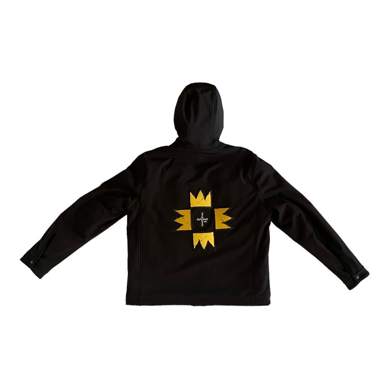 Puede incluir: Chaqueta negra con capucha y un dise&ntilde;o bordado en dorado en la espalda. El dise&ntilde;o presenta una cruz con una corona en cada punto.