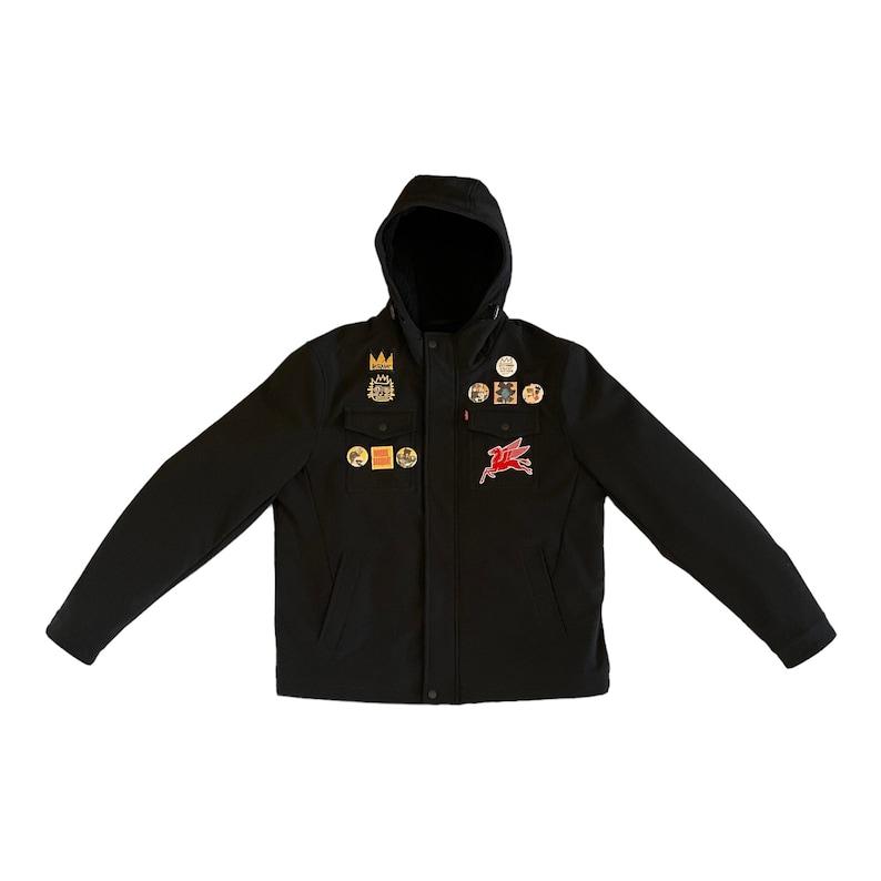 Puede incluir: Una chaqueta negra con capucha, cierre de cremallera y varios parches, entre ellos un caballo alado rojo, una corona y varios dise&ntilde;os m&aacute;s.