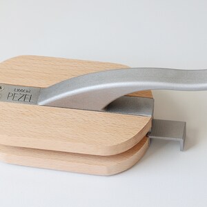 Puede incluir: Un cascanueces de madera con un mango plateado. El cascanueces est&aacute; etiquetado como "PEZEL E100C 101".