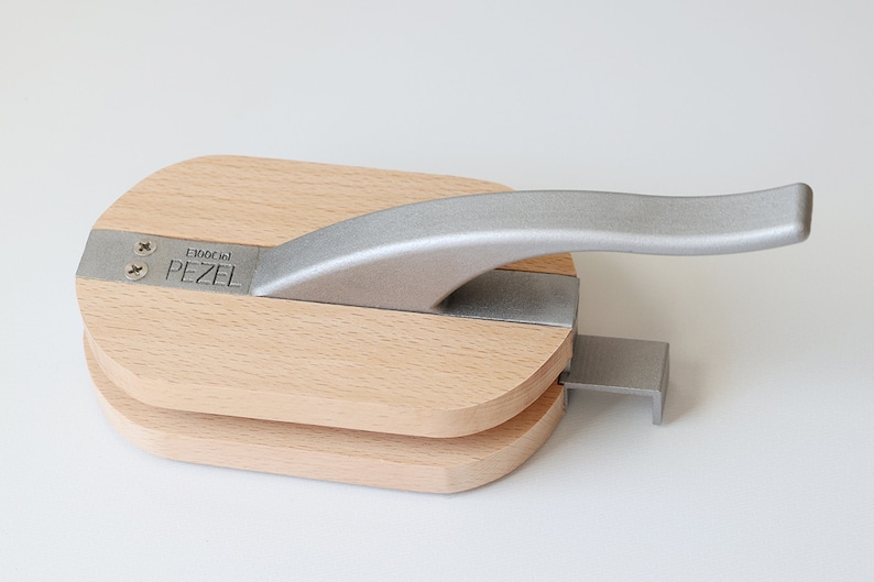 Puede incluir: Un cascanueces de madera con un mango plateado. El cascanueces est&aacute; etiquetado como "PEZEL E100C 101".