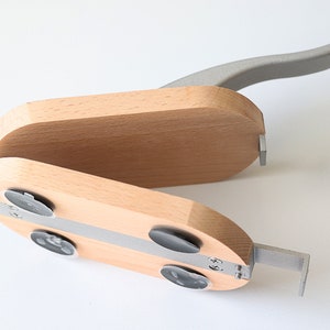 Puede incluir: Un cascanueces de madera con un mango de metal gris. El cascanueces tiene una tira de metal plateada y cuatro pies de goma negra.