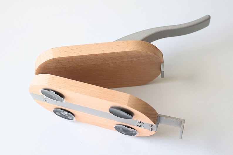 Puede incluir: Un cascanueces de madera con un mango de metal gris. El cascanueces tiene una tira de metal plateada y cuatro pies de goma negra.