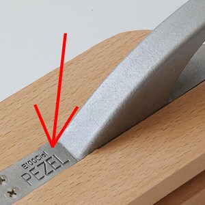 Puede incluir: Primer plano de una herramienta de madera con un mango de metal plateado. La herramienta est&aacute; etiquetada como "Pezel E100Cial".