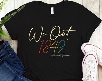 May include: Black t-shirt with the text "We Out. 1849" in colorful lettering and the signature "Harriet Tubman" underneath.