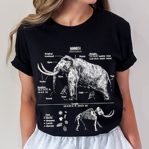 May include: Black t-shirt with a white graphic of a mammoth with anatomical labels. The graphic includes the mammoth's height, weight, length, diet, and skeletal structure. The text on the shirt reads "MAMMOTH (Mammuthus)"