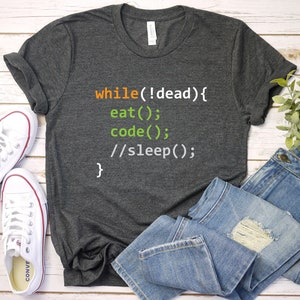 May include: A dark gray t-shirt with the text "while(!dead) { eat(); code(); //sleep(); }" printed on it in orange, green, and white.