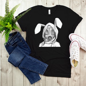 K&ouml;nnte beinhalten: Schwarzes T-Shirt mit einem Aufdruck einer Person mit Gasmaske und Hasenohren.