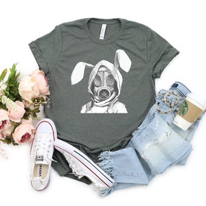 K&ouml;nnte beinhalten: Ein dunkelgr&uuml;nes T-Shirt mit einem wei&szlig;en Aufdruck eines Kaninchens, das eine Gasmaske tr&auml;gt. Das Kaninchen hat wei&szlig;e Ohren und tr&auml;gt einen wei&szlig;en Kapuzenpullover.