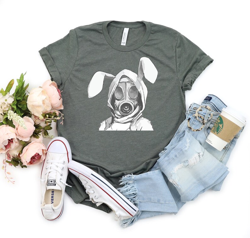 K&ouml;nnte beinhalten: Ein dunkelgr&uuml;nes T-Shirt mit einem wei&szlig;en Aufdruck eines Kaninchens, das eine Gasmaske tr&auml;gt. Das Kaninchen hat wei&szlig;e Ohren und tr&auml;gt einen wei&szlig;en Kapuzenpullover.