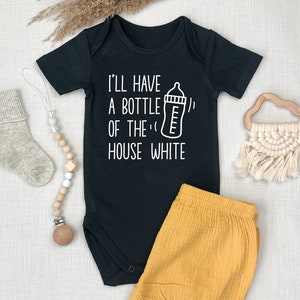 以下が含まれることがあります： 白い文字で「I'll have a bottle of the house white」と書いてあり、赤ちゃん用の哺乳瓶のイラストが描かれた黒いベビーロンパース。ロンパースはマスタードイエローのベビーショーツと組み合わされています。