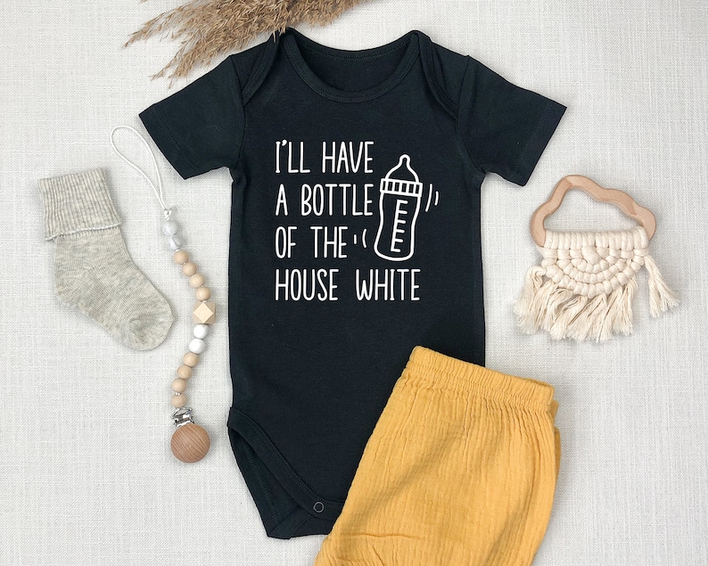 以下が含まれることがあります： 白い文字で「I'll have a bottle of the house white」と書いてあり、赤ちゃん用の哺乳瓶のイラストが描かれた黒いベビーロンパース。ロンパースはマスタードイエローのベビーショーツと組み合わされています。