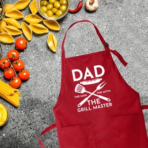 May include: Red apron with white text that reads "Dad The Man The Myth The Grill Master" with a grill spatula and fork graphic.