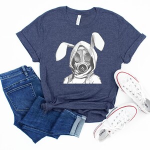 K&ouml;nnte beinhalten: Ein marineblaues T-Shirt mit einem wei&szlig;en Aufdruck eines Kaninchens, das eine Gasmaske tr&auml;gt. Das Kaninchen hat lange Ohren und tr&auml;gt einen Kapuzenpullover.