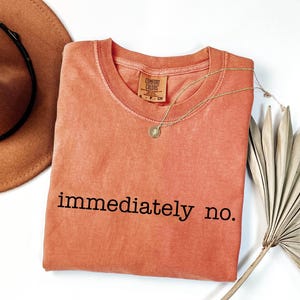 May include: A coral colored t-shirt with the text "immediately no." printed in black.