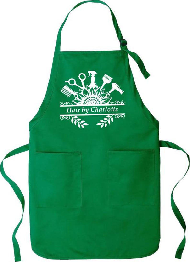 May include: Green apron with two front pockets and a neck strap. The apron features a white graphic of salon tools and the text "Hair by Charlotte". The design includes scissors, a comb, a spray bottle, and a hairdryer.