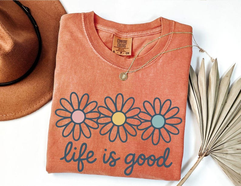 a red t-shirt with a flower design and the text "life is good" printed on it, along with a brown hat and a fan.