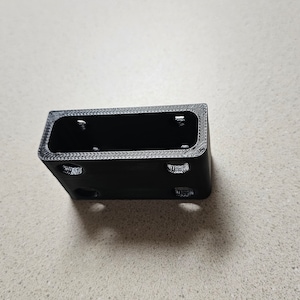 May include: Black plastic 3D printed box with a rectangular opening and several small holes on the sides.