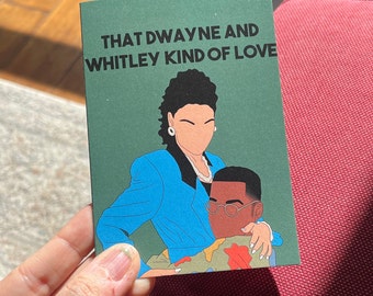 May include: A green card with the text "That Dwayne and Whitley kind of love" in black lettering. The card features an illustration of a woman with dark hair wearing a blue blazer and a man with brown hair wearing a camouflage shirt.