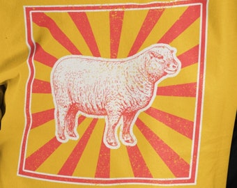 May include: A yellow t-shirt with a vintage-style graphic of a sheep in a red and yellow sunburst design. The text "wear with pride designs" is at the bottom of the image.