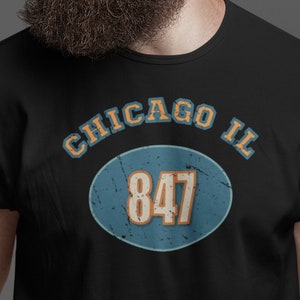 May include: Black t-shirt with a blue and orange circle graphic that says "CHICAGO IL 847" in white text.