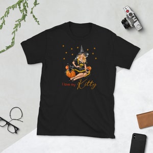 May include: Black t-shirt with a graphic of a witch sitting on pumpkins. The witch is wearing a black dress and a pointed hat. The text "I love my Kitty" is printed below the graphic.