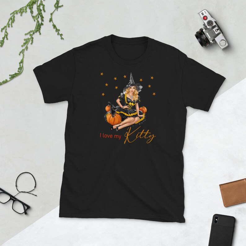 May include: Black t-shirt with a graphic of a witch sitting on pumpkins. The witch is wearing a black dress and a pointed hat. The text "I love my Kitty" is printed below the graphic.