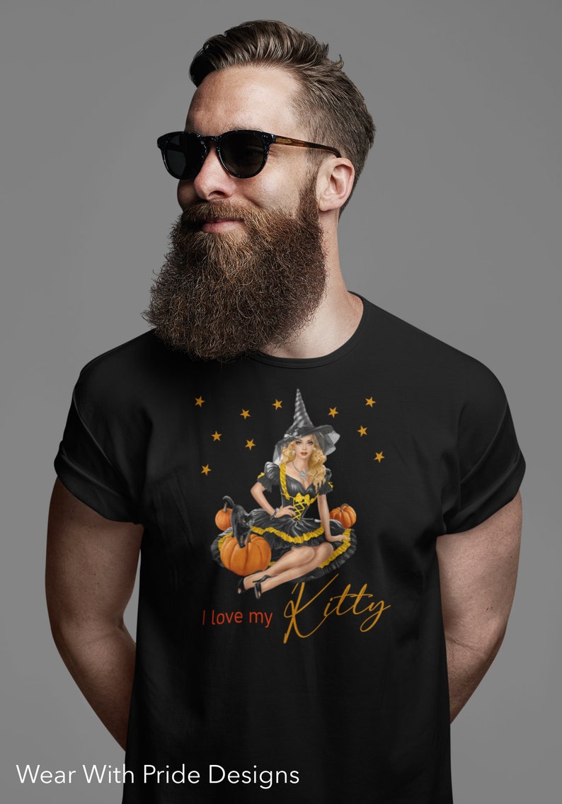 May include: Black t-shirt with a graphic of a witch sitting on pumpkins with a black cat. The text "I love my Kitty" is printed on the shirt.