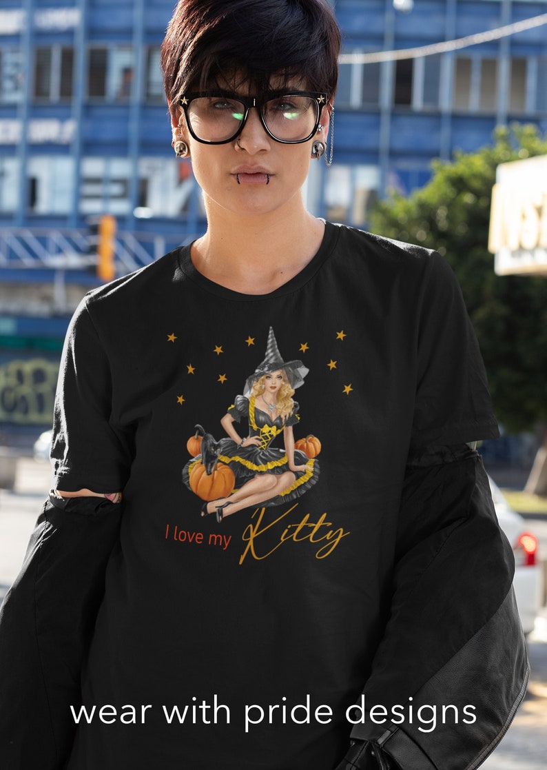 May include: Black t-shirt with a graphic of a witch sitting on pumpkins. The witch is wearing a black dress with a yellow belt and a black hat. The text "I love my Kitty" is printed below the graphic.