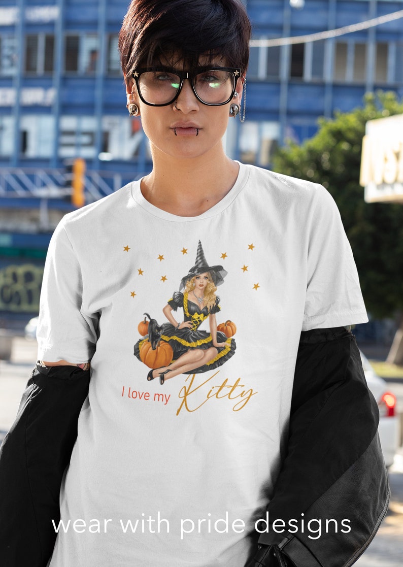 May include: White t-shirt with a graphic of a witch in a black dress and hat sitting on pumpkins with a black cat. The text "I love my Kitty" is printed on the shirt.