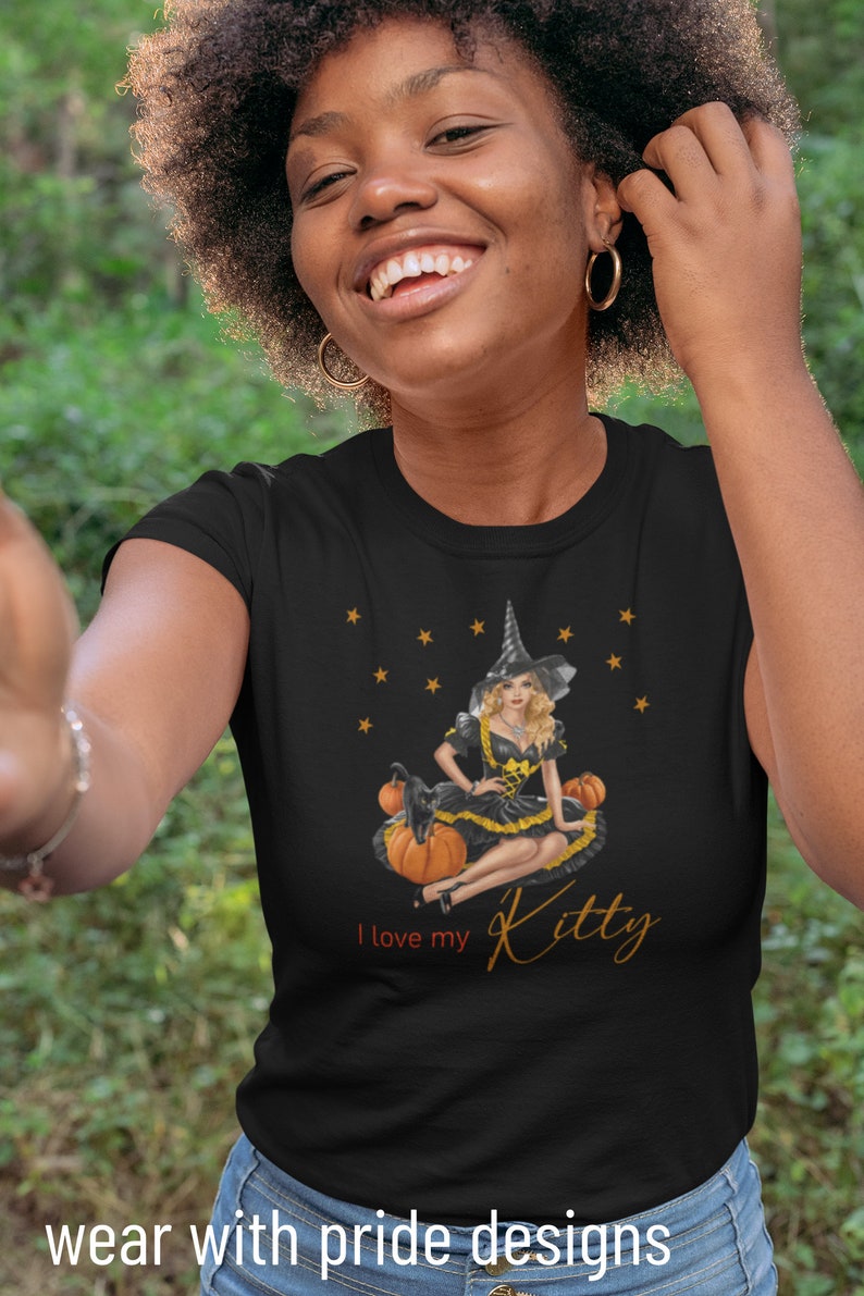 May include: Black t-shirt with a graphic of a witch sitting on pumpkins with a black cat. The text "I love my Kitty" is printed on the shirt.