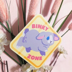 May include: A yellow and orange diamond-shaped sticker with the text "Binky Zone" and a cartoon illustration of a gray bunny rabbit with blue eyes.