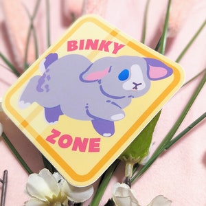 May include: A yellow and orange sticker with a gray rabbit and the text "BINKY ZONE" in pink letters.