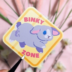 May include: A yellow diamond-shaped sticker with a gray bunny rabbit and the text "BINKY ZONE" in pink letters.