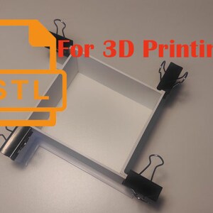 Puede incluir: Una caja blanca de cuatro lados, unida por clips. La caja está etiquetada "STL" para impresión 3D.
