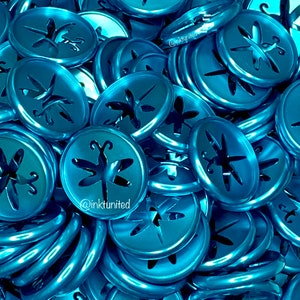 May include: A pile of shiny, teal-colored metal discs. Each disc has a dragonfly-shaped cutout in the center. The discs are stacked and scattered, creating a textured surface. The watermark "@inkunited" is visible on some discs.
