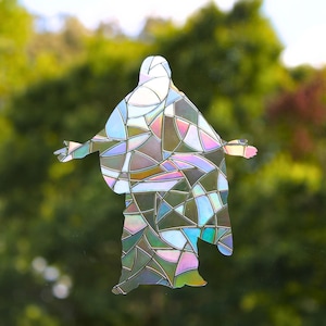 May include: A window decal featuring a silhouette of a figure with arms outstretched, designed with a geometric stained glass pattern. The surface displays an iridescent, holographic finish that reflects various colors across its segmented sections.