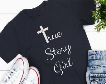 May include: Navy blue t-shirt with a white cross and the words "True Story Girl" in a script font. White canvas sneakers with red trim and denim shorts are also in the image.