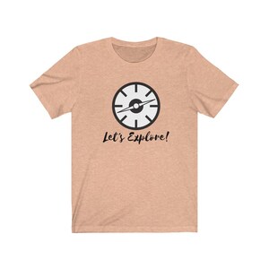 May include: A light peach colored t-shirt with a black compass graphic and the text "Let's Explore!" printed on the front.