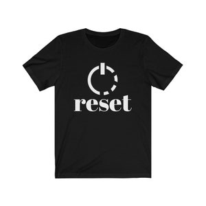 May include: Black t-shirt with a white graphic of a power button symbol and the word "reset" in a clean, sans-serif font. The shirt is made of a soft material and has short sleeves.