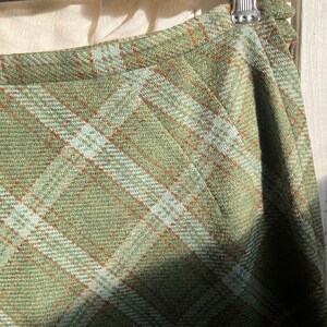 Puede incluir: Una falda de cuadros verdes con un patr&oacute;n de cuadros marrones y blancos. La falda est&aacute; hecha de una tela suave y tejida.