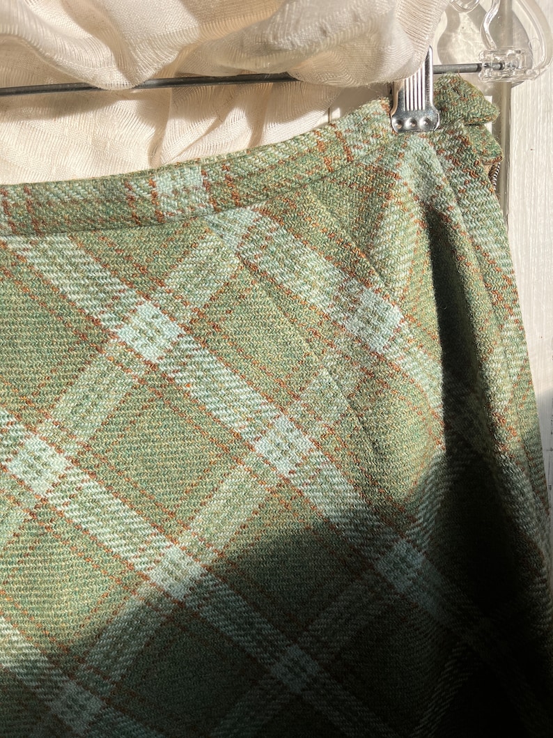 Puede incluir: Una falda de cuadros verdes con un patr&oacute;n de cuadros marrones y blancos. La falda est&aacute; hecha de una tela suave y tejida.