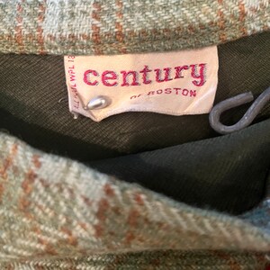 Puede incluir: Primer plano de una tela de cuadros verde y marr&oacute;n con una etiqueta blanca que dice "century of boston" en letras rojas.