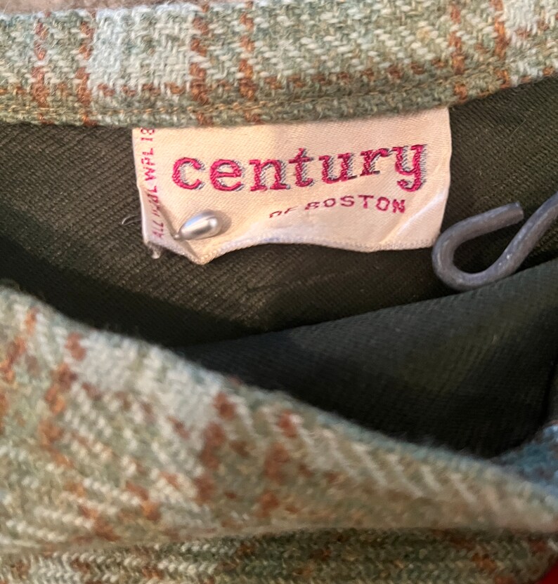 Puede incluir: Primer plano de una tela de cuadros verde y marr&oacute;n con una etiqueta blanca que dice "century of boston" en letras rojas.